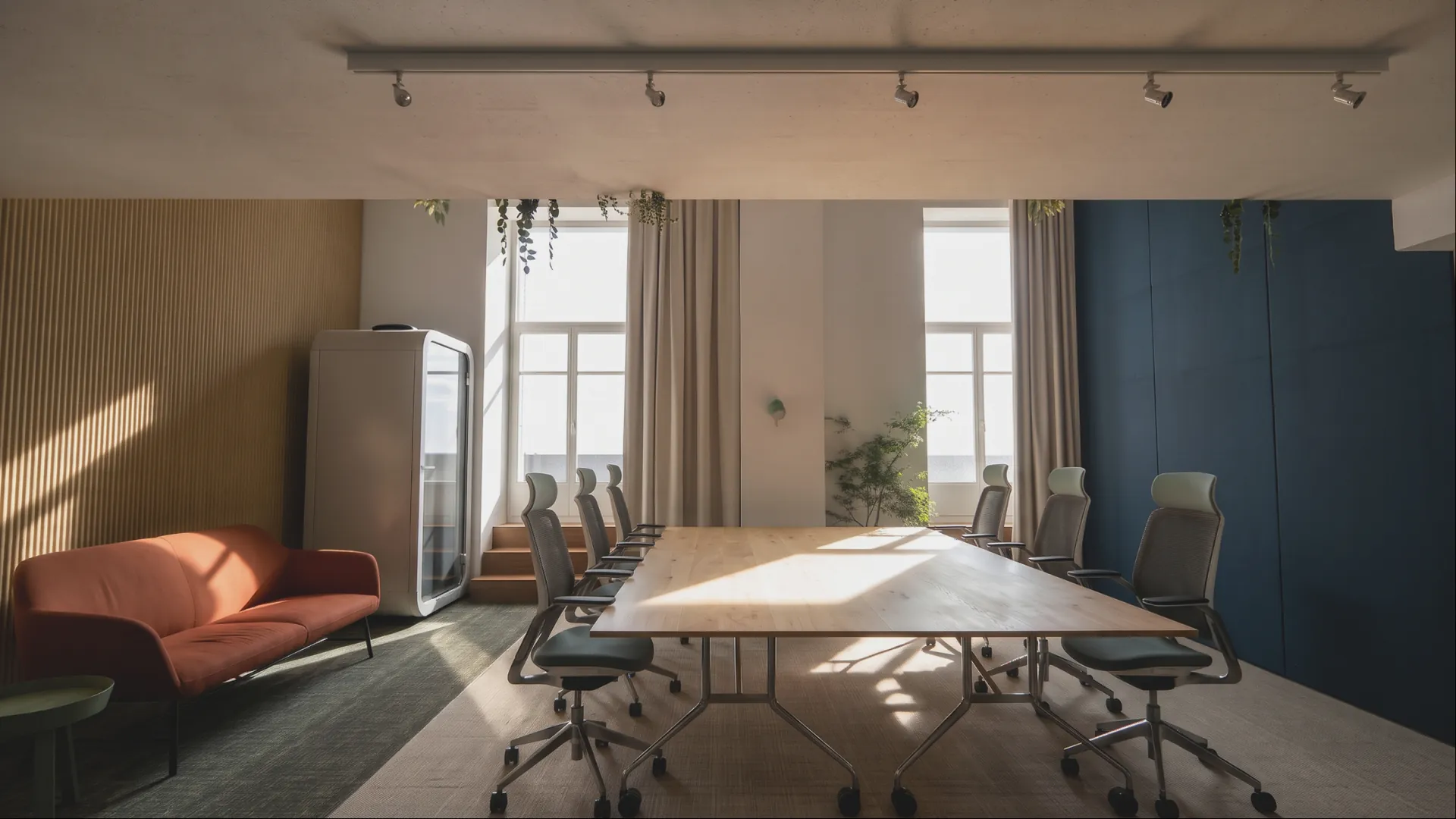 A meeting room with a long table, task chairs, a blue wall and a rust sofa